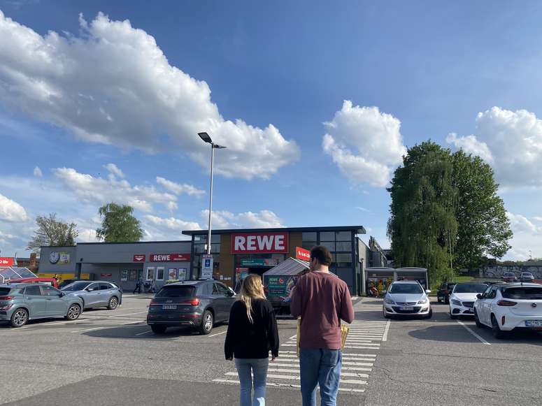 "Zwei Personen auf dem REWE-Parkplatz."
