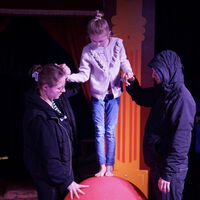 "Ava balanciert im Zirkus auf einem Ball, gesichert von zwei anderen Personen"