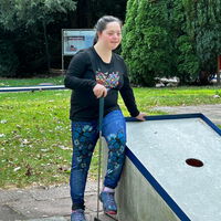 "Maya sitzt beim Minigolfen auf der Kante eines Parcours."