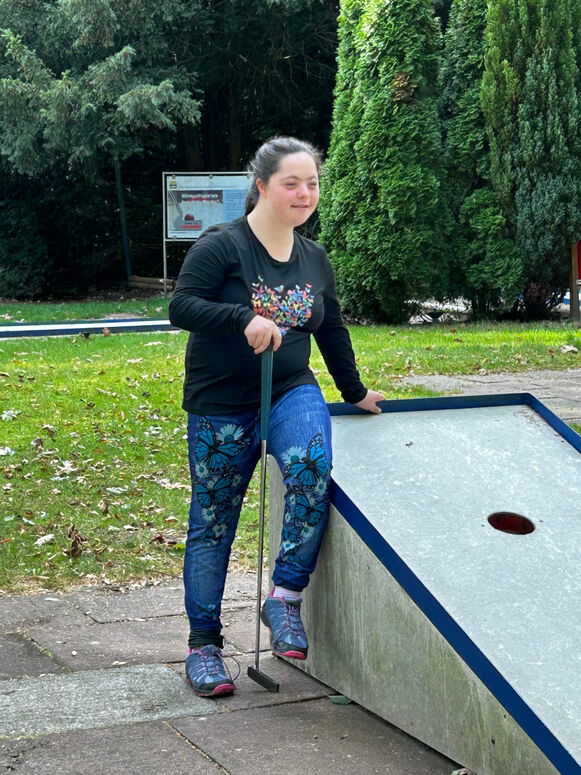 "Maya sitzt beim Minigolfen auf der Kante eines Parcours."