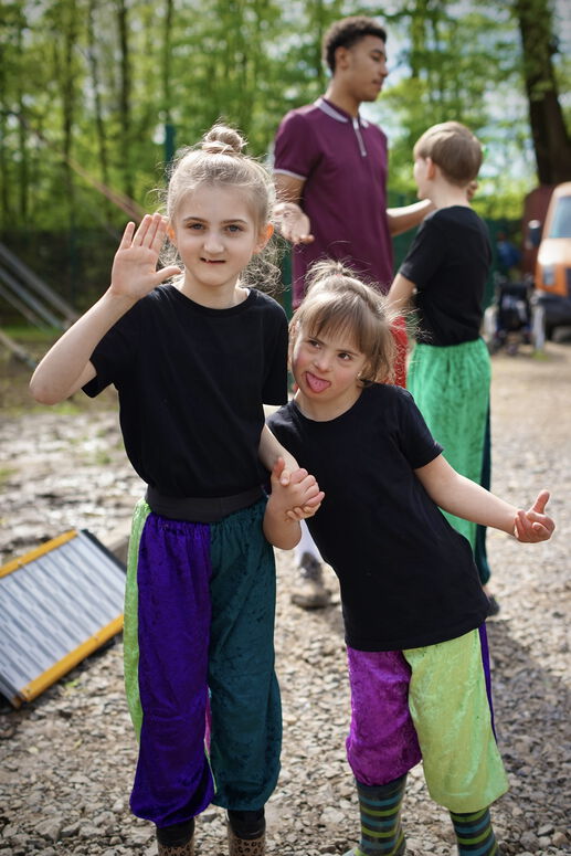 "Ava und ein anderes Kind in Zirkusoutfit winken in die Kamera"